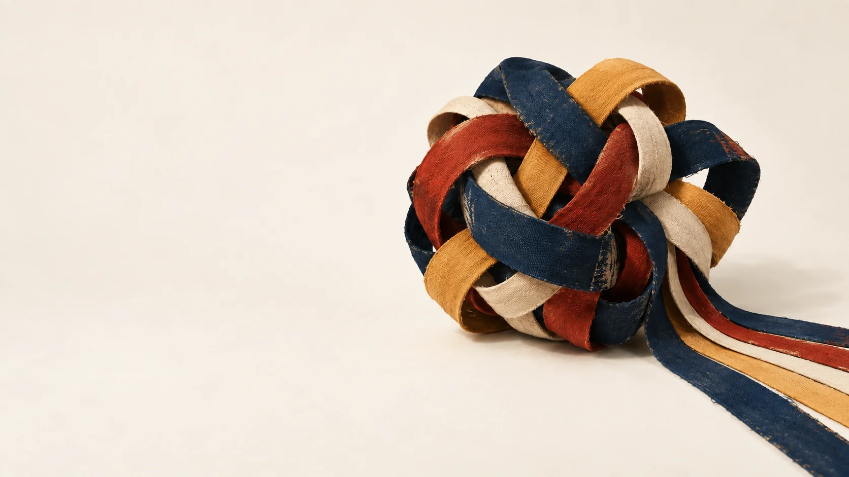 Navy, red, and ochre fabric ribbons untangling across a warm studio surface.